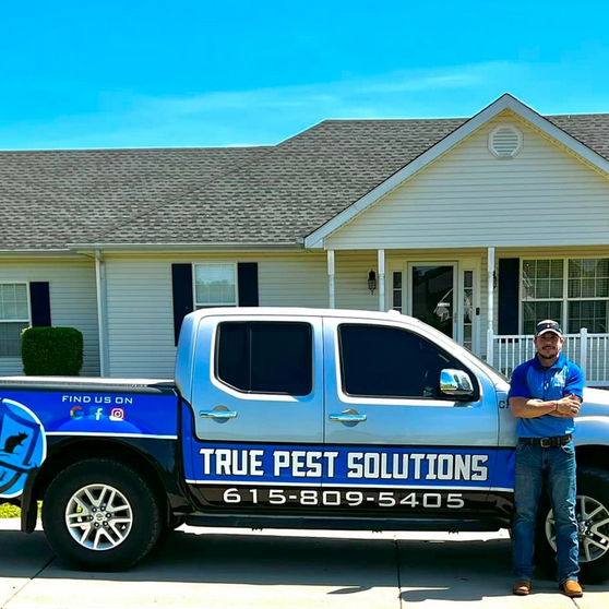 Josh Gallas, owner and operator of True Pest Solutions, stands in front of truck at client's home providing pest control services